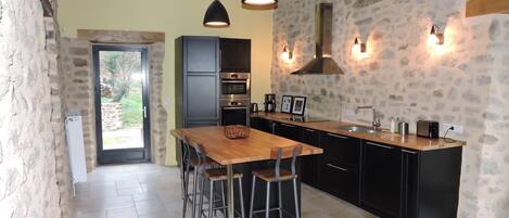 A modern kitchen with a wooden dining table, black cabinets, and stone walls.