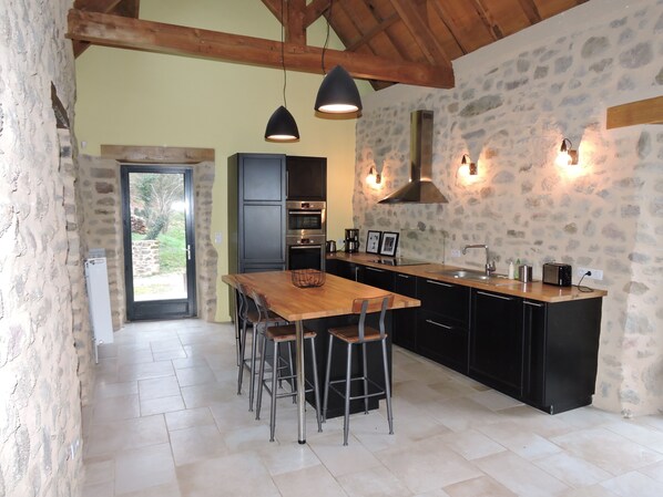 A modern kitchen with a wooden dining table, black cabinets, and stone walls.