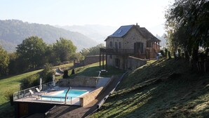 Una casa de piedra con piscina y zona de estar al aire libre, en un paisaje montañoso.