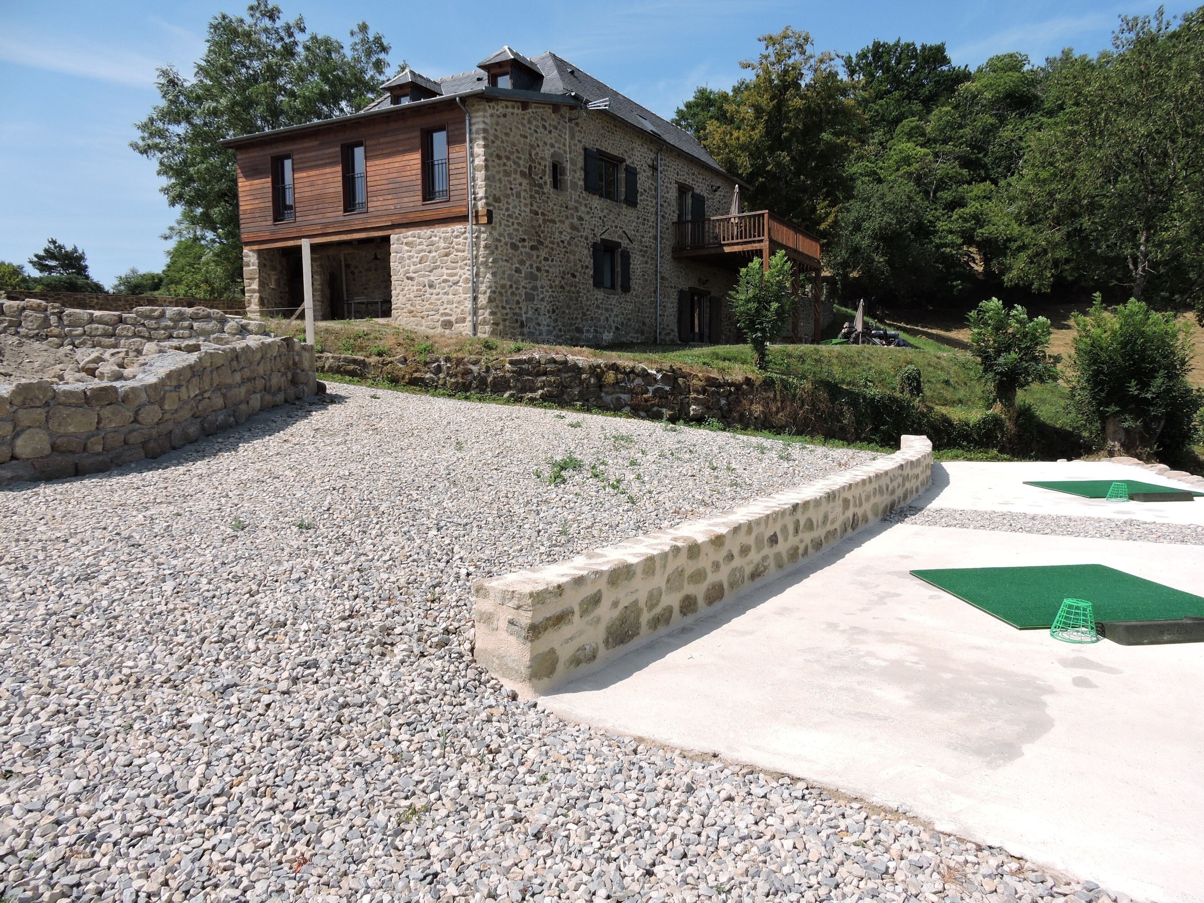 Une maison en pierre avec un étage supérieur en bois, un mur de soutènement en pierre et une allée gravillonnée.