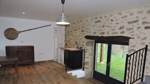 Een ruime woonkamer met houten vloer, een eettafel, een hanglamp en uitzicht door een glazen deur op een tuin.