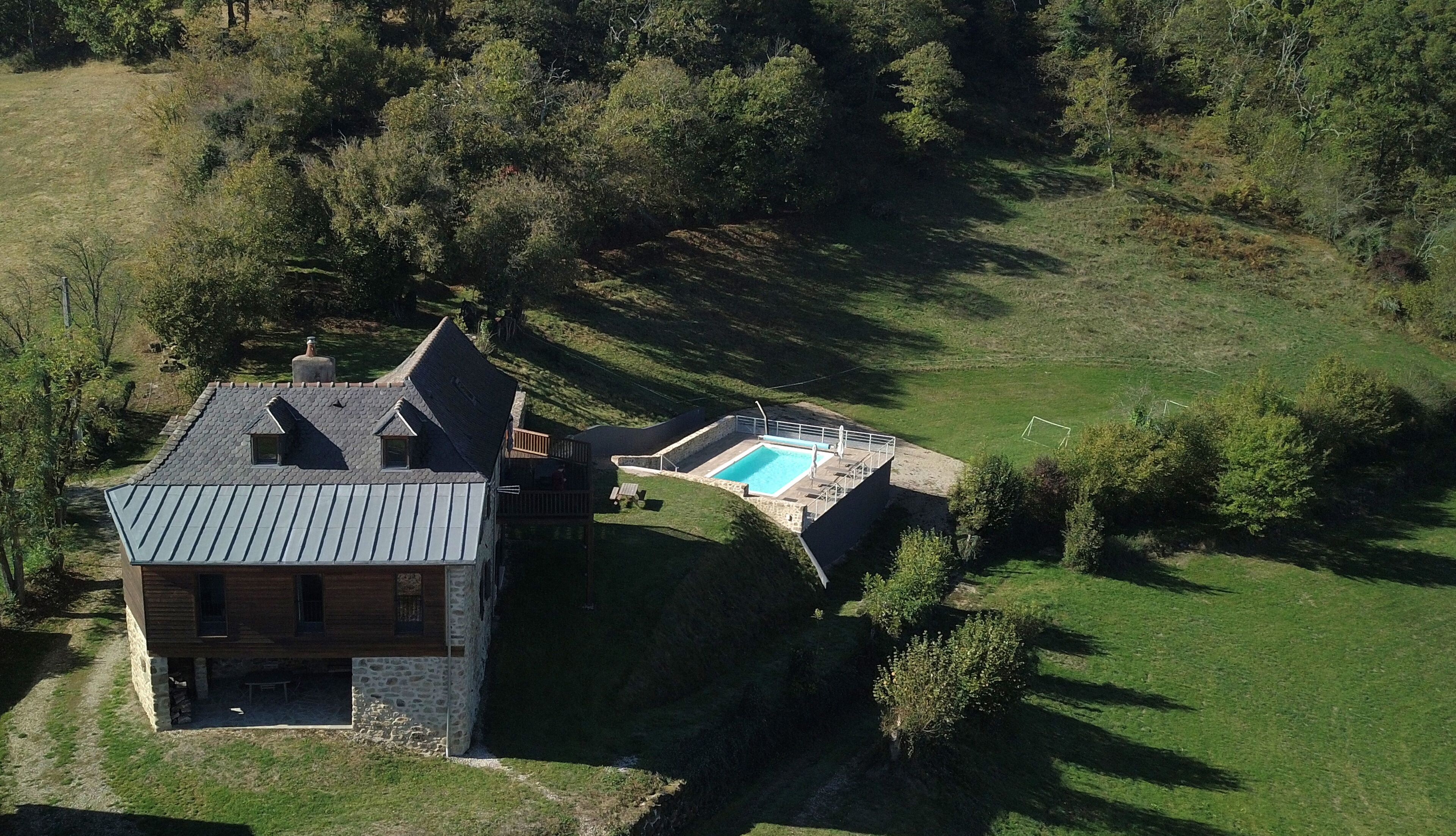 Una casa de pedra amb piscina, envoltada d'un paisatge herbaci i arbres.