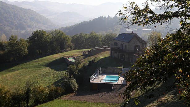 Una casa con piscina, rodeada de abundante vegetación y colinas al fondo.
