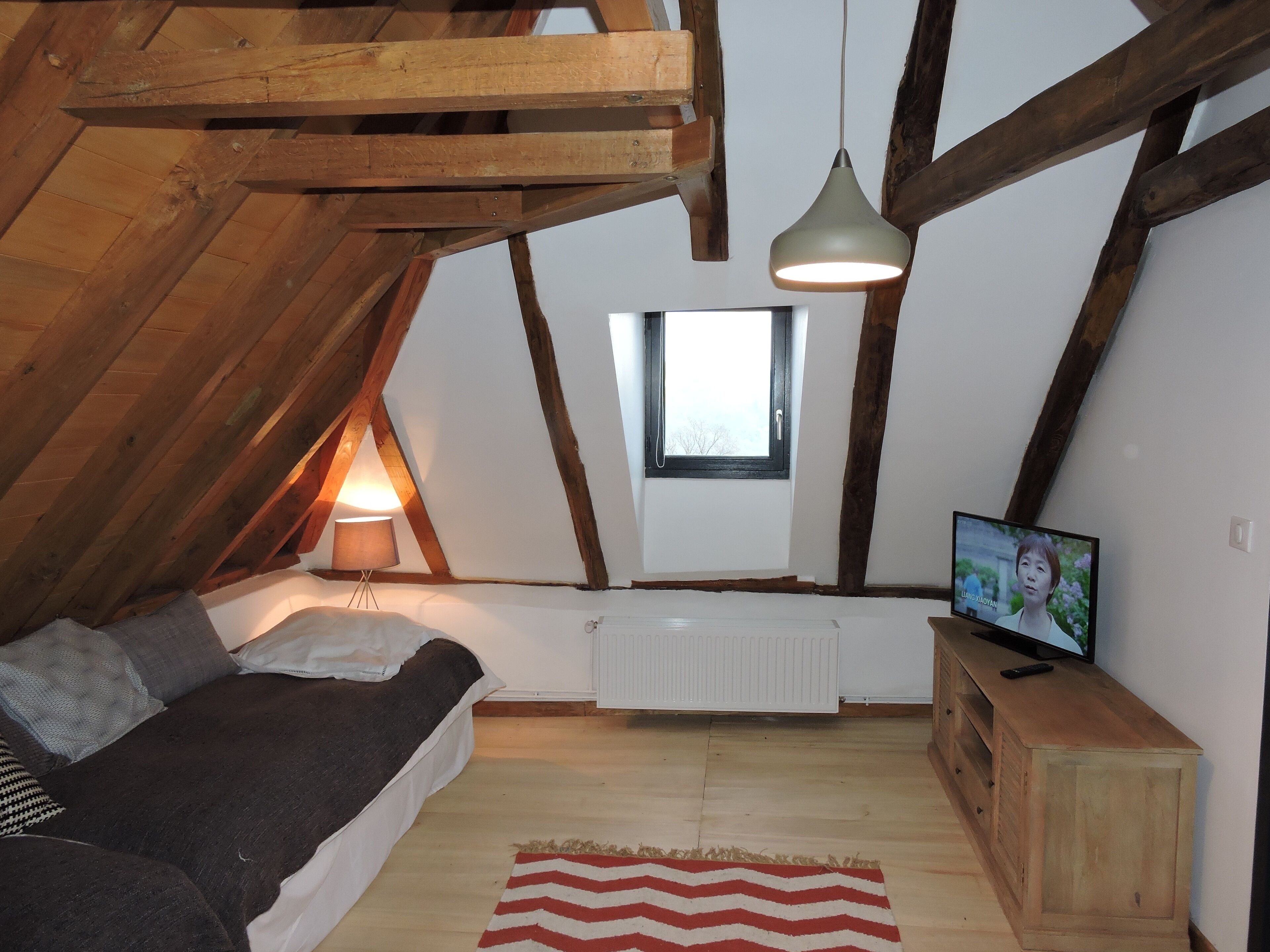 A cozy attic bedroom with a bed, a TV, and a window.