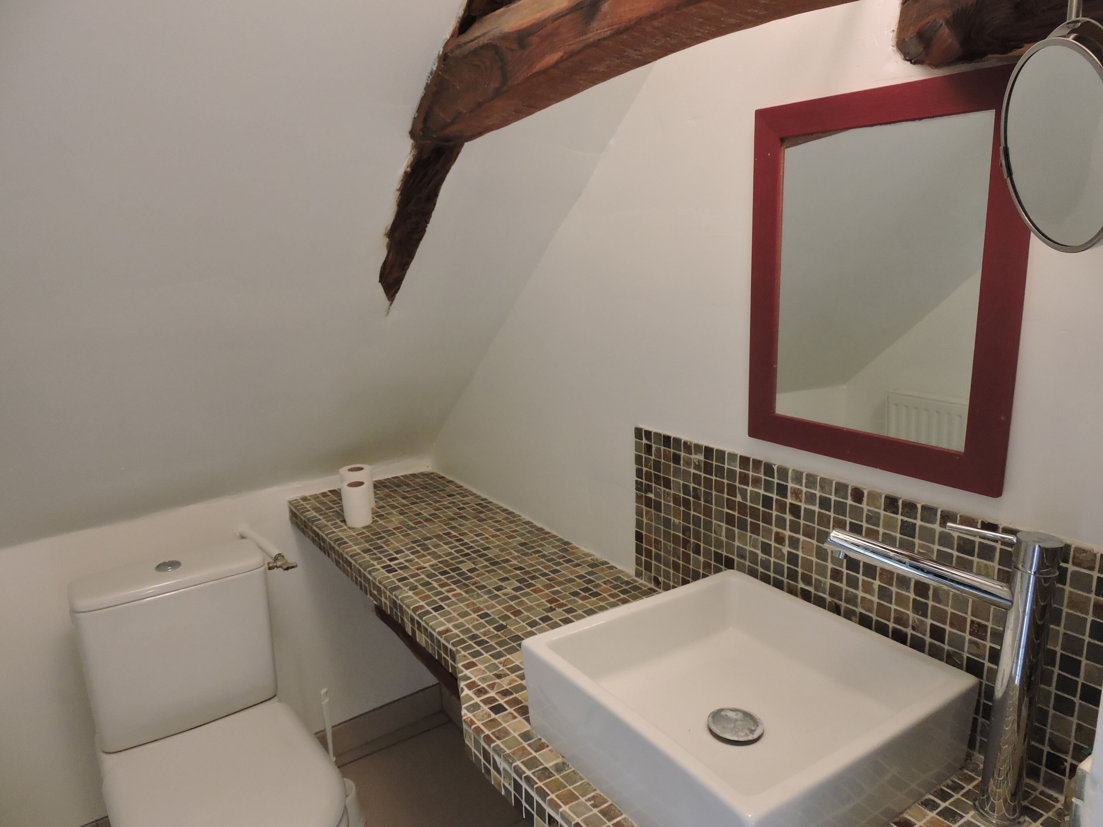 Ein Badezimmer mit Toilette, Waschbecken und Spiegel sowie einer gefliesten Rückwand.