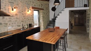 Una cocina con una isla de madera, armarios negros, paredes de piedra y una escalera que lleva a un nivel superior.