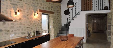Una cocina con una isla de madera, armarios negros, paredes de piedra y una escalera que lleva a un nivel superior.
