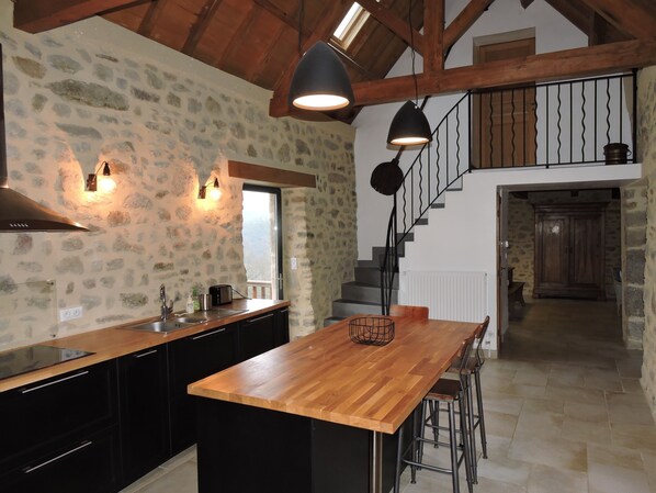 A kitchen with a wooden island, black cabinets, stone walls, and a staircase leading to an upper level.