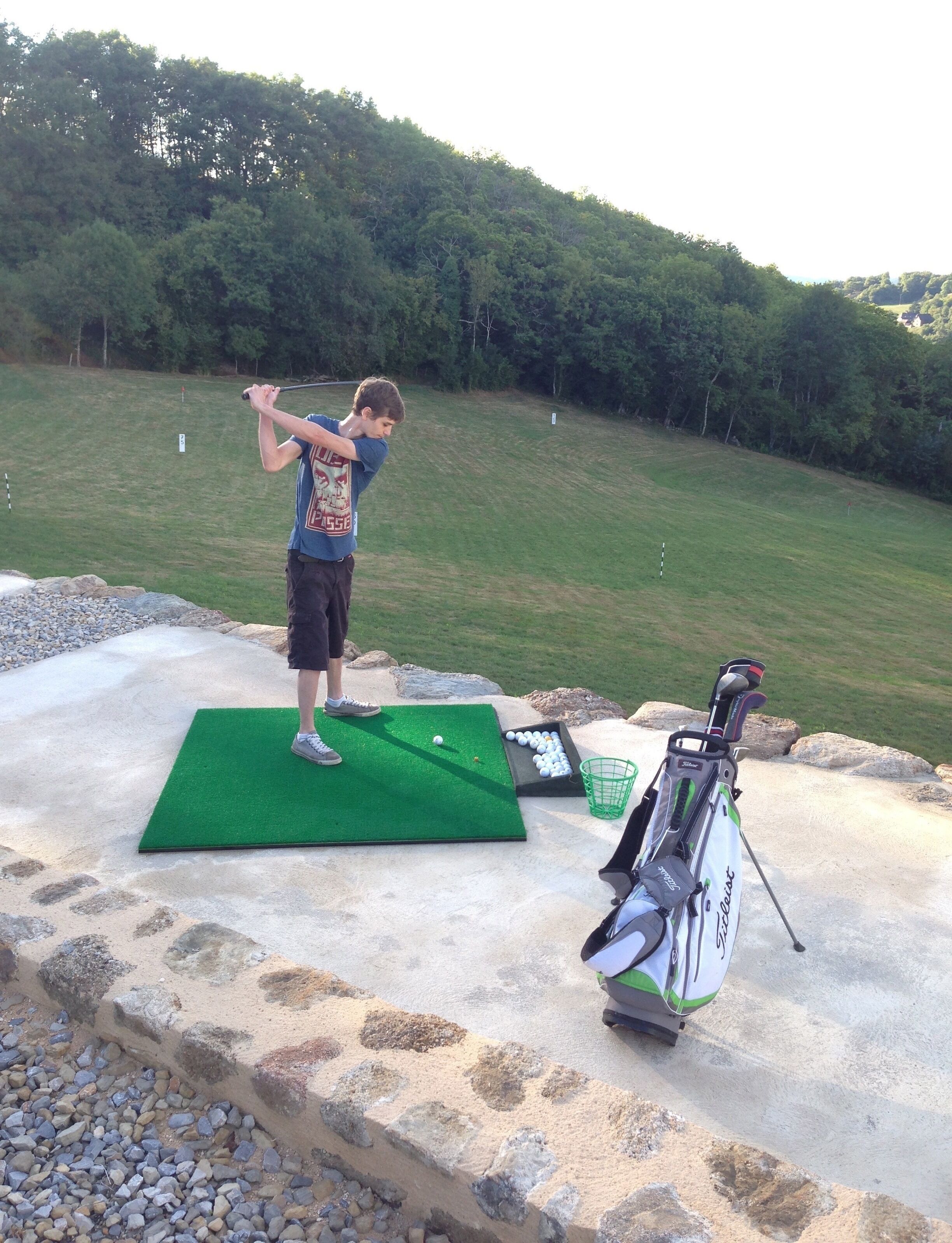 A person practicing golf on a mat with a golf bag nearby.