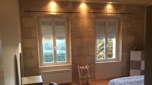 Une chambre avec deux fenêtres, un lit, une chaise et un bureau.