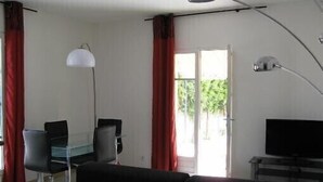 A modern living room with a sofa, a desk with a chair, a television, and a large window with curtains. - 400m to the center of Uzès, appartment for 4 people (Uz ès)