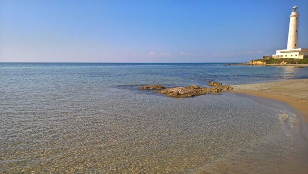Une plage dégagée, avec un phare et un affleurement rocheux dans l’eau.