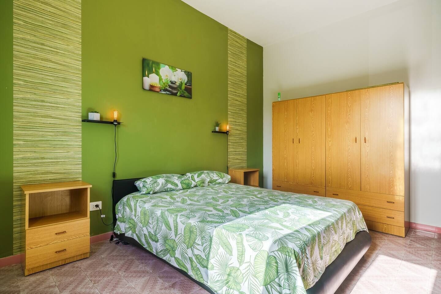 A bedroom with a bed, wooden wardrobe, green walls, and a painting of flowers.
