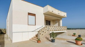 Un bâtiment moderne doté d ’un toit plat, d’un balcon avec une balustrade à treillis et d’un escalier menant à l’entrée. Des plantes en pot sont disposées au niveau du sol.