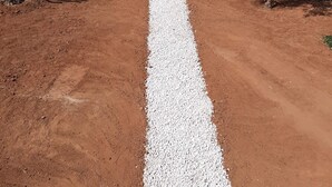 Un chemin de terre, avec une allée de gravier blanc qui mène à un bâtiment doté d’une piscine.