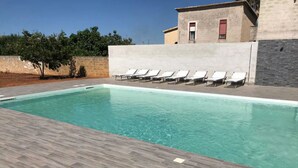 Une piscine rectangulaire avec une terrasse carrelée, entourée de chaises longues.