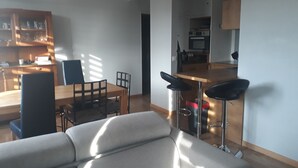 Ein modernes Wohnzimmer mit einer Couch, einem Esstisch mit Stühlen und einer Küchenzeile mit Barhocker.
