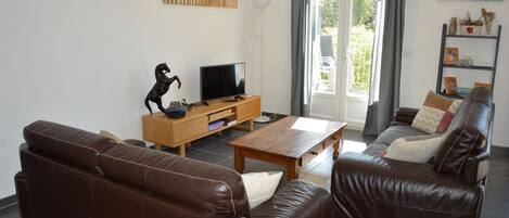 A living room with two brown leather sofas, a wooden coffee table, a TV on a wooden stand, and a painting of a pier on the wall.