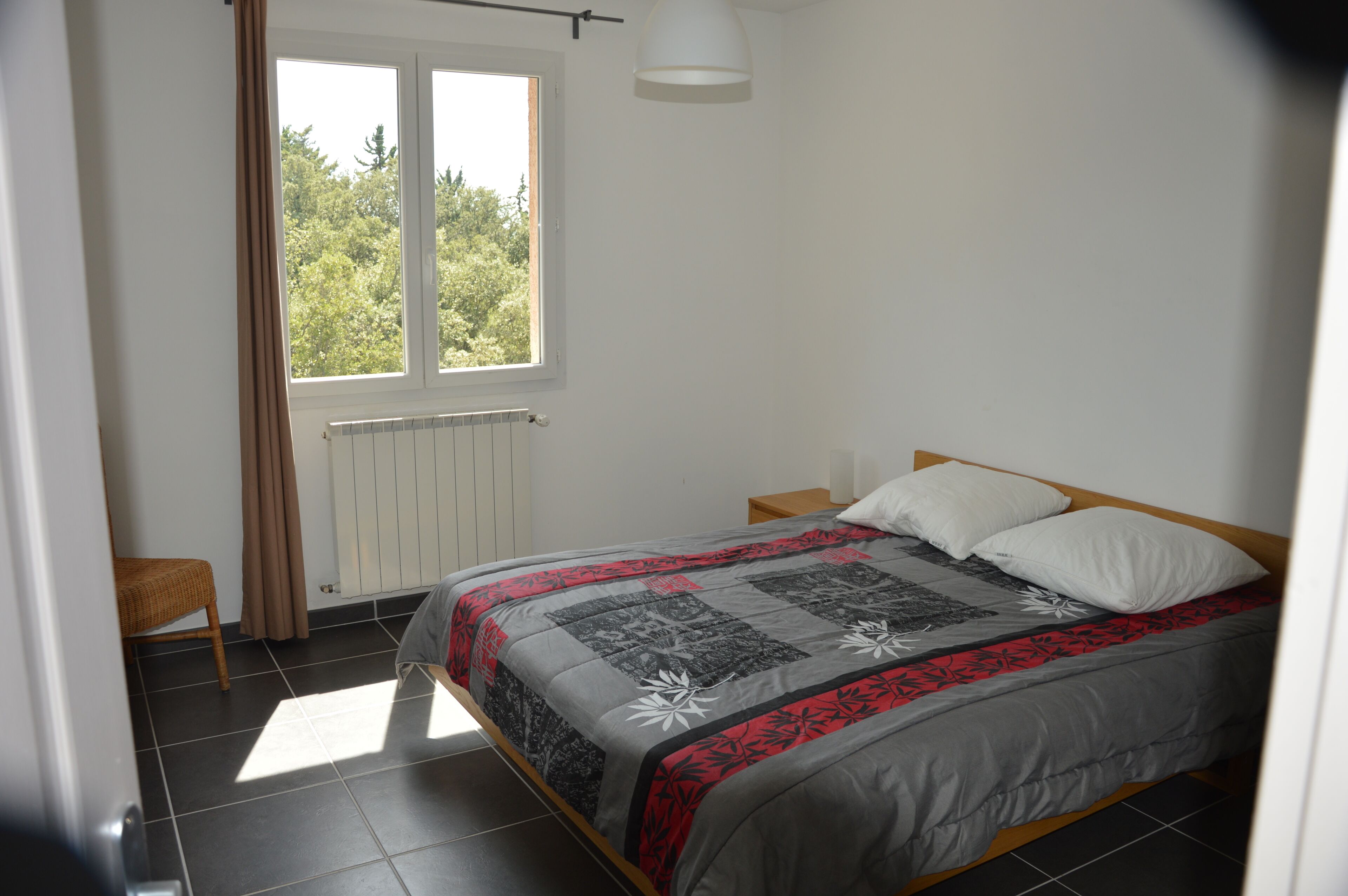 A bedroom with a bed, a window, a radiator, and a chair.
