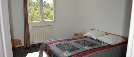 A bedroom with a bed, a window, a radiator, and a chair.