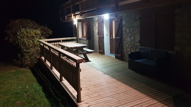 Een houten terras met een tafel, stoelen en een bank, plus een stenen muur.
