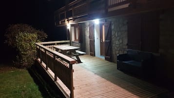 Une terrasse en bois avec une table et des chaises, un mur en pierre et un canapé.