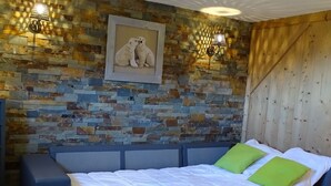 Een slaapkamer met een stenen muur, een bed met witte beddengoed en groene kussens, een blauwe bank en twee wandlampen.