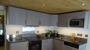 Een kleine keuken met grijze kastjes, roestvrijstalen apparatuur en een houten plafond.