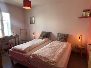 A room with two beds, a desk, a chair, a ladder, and a shelf with books.