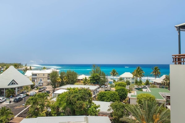 A coastal view with buildings, palm trees, and the ocean. - Bienvenue location offers this T4 Duplex on the beach of Roches Noires sea view (Saint-Gilles les Bains)