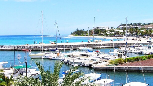 Un port de plaisance avec des bateaux amarrés, une plage en arrière-plan et un ciel dégagé.