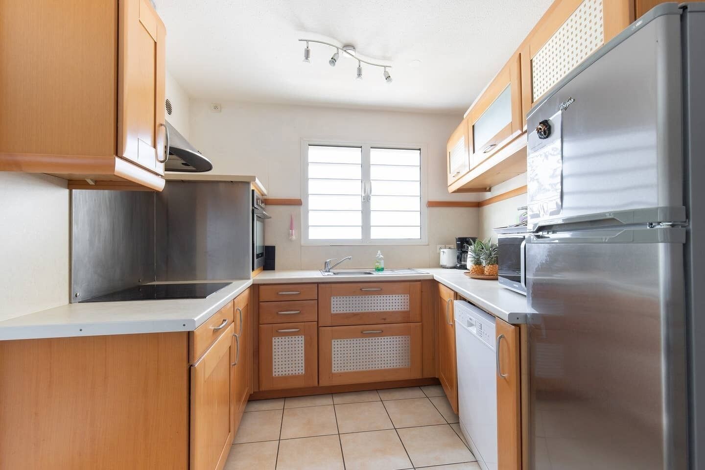 A compact kitchen with wooden cabinets, a stainless steel refrigerator, and a window providing natural light.