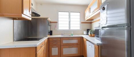 A compact kitchen with wooden cabinets, a stainless steel refrigerator, and a window providing natural light.