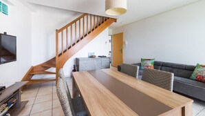Un salon moderne avec un escalier en bois, une table à manger et un canapé agrémenté de coussins colorés.
