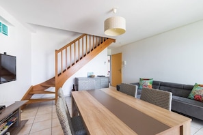 A modern living room with a wooden staircase, a dining table, and a sofa with colorful cushions.