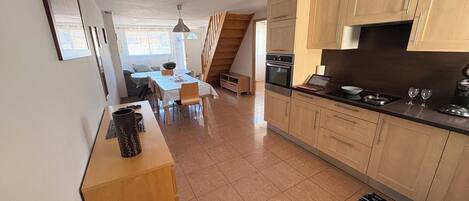 A modern kitchen with wooden cabinets, a dining area with a table and chairs, and a staircase leading to another level.