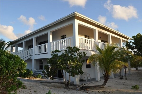 A two-story building with a balcony on the second floor, surrounded by palm trees and a sandy ground. - BOOK NOW Lower Rates! Private Beachfront Villa, Full Laundry, Kitchen, WiFi & AC (Whitby)