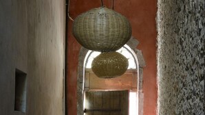 A narrow hallway with a large woven basket hanging from the ceiling, a metal trash bin, and a wooden door at the end.