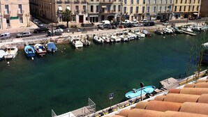 A marina with boats docked, a street with buildings, and a clear sky.