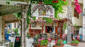 Un espace extérieur aménagé avec des tables et des chaises, une enseigne indiquant un établissement proposant une cuisine traditionnelle, et des plantes en pot.
