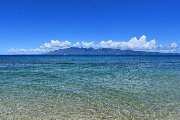 A clear view of a beach with shallow water and a mountain in the distance.