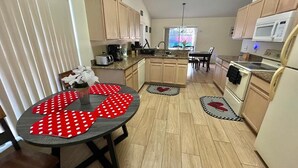 Een kleine keuken met houten kastjes, een eettafel met rode stippeldeken en een magnetron.