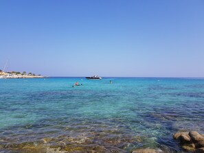 A coastal scene with clear turquoise waters, rocky shoreline, and a distant yacht. - Air-conditioned house with sea view, 80 metres from the beach (Lumio)