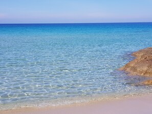 A clear view of a beach with calm waters and a rocky outcrop.