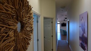 A hallway with a wooden wall art piece, a ceiling light, and a poster on the wall. - Beachfront Condo With Panoramic Views of the Gulf Plus Beach Gear, Grill & Wifi (Indian Rocks Beach)
