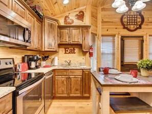 A wooden cabin-style kitchen with wooden cabinets, a granite countertop, a stove, a sink, and a dining area with a table and chairs.