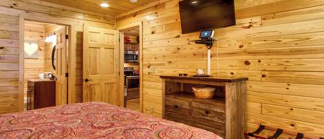 A wooden cabin room with a bed, a ceiling fan, a TV, and a small kitchenette.