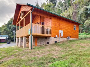 A wooden cabin with a balcony, stone foundation, and a green roof.