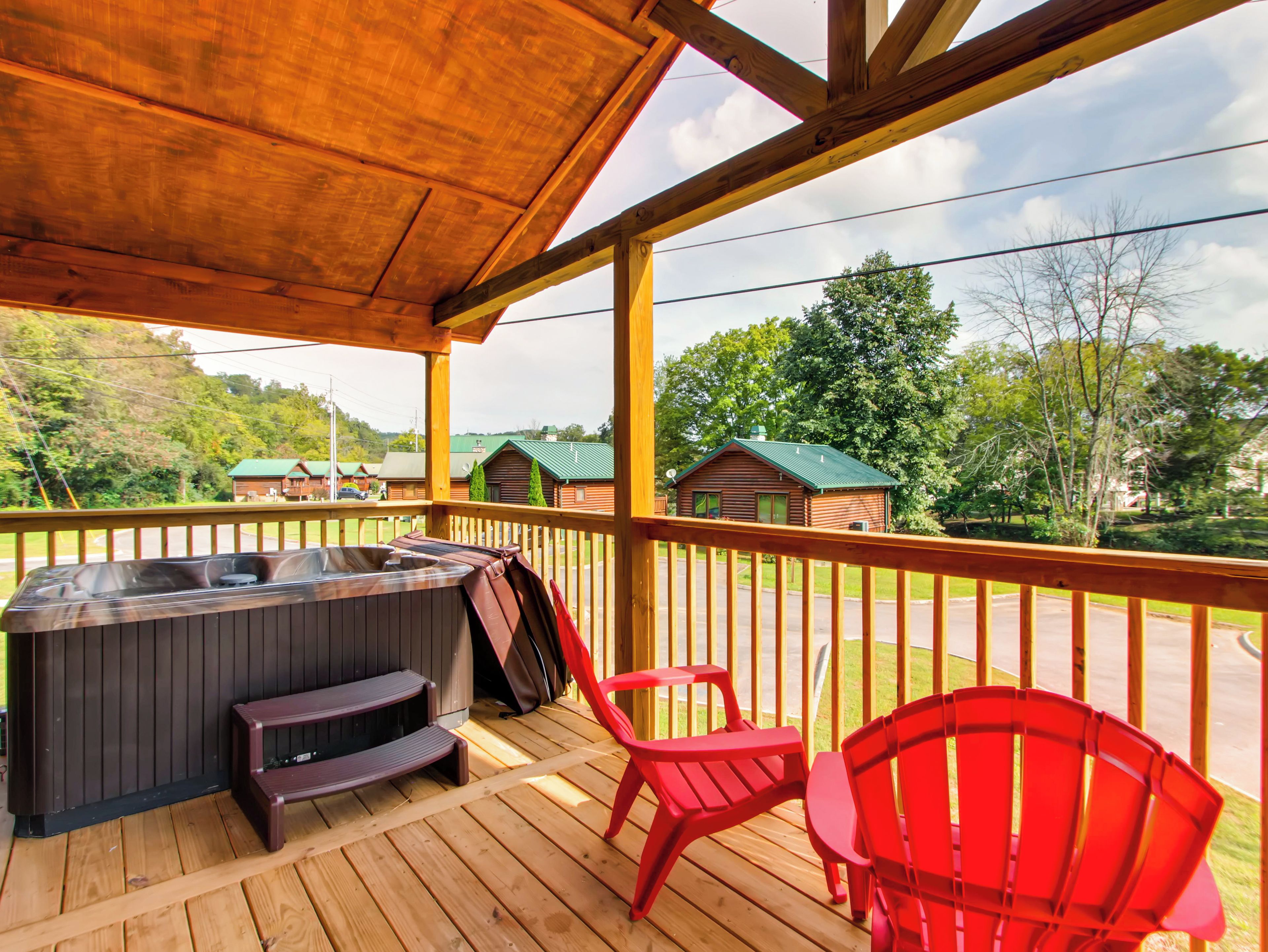 Una terraza de madera con un jacuzzi, sillas rojas y vistas a un paisaje verde con edificios.