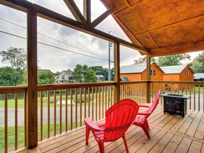 A wooden deck with a covered area, red chairs, and a black grill.